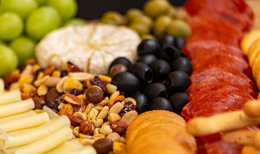 A charcuterie board with cheese, olives, nuts, and grapes