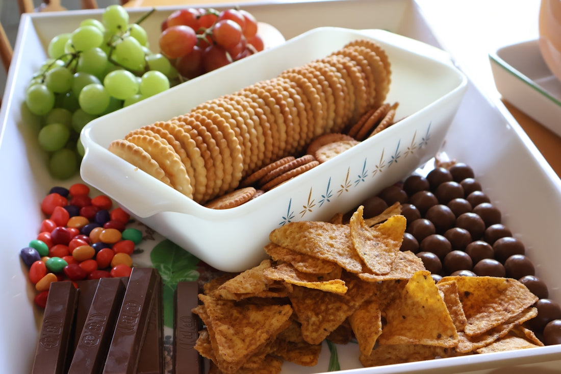 A platter of assorted snacks including grapes, crackers, and chocolate.