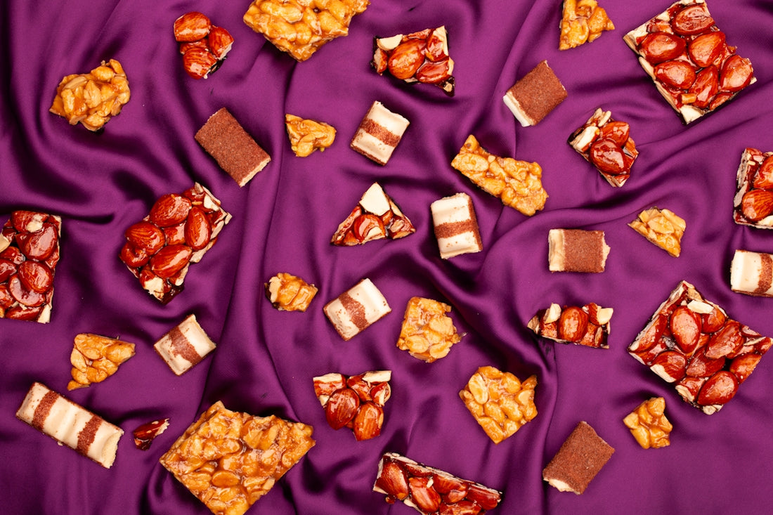 Assortment of chocolate bars and peanut brittle on purple silk.