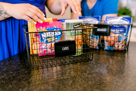 Hands organizing snacks into wire baskets on a countertop.